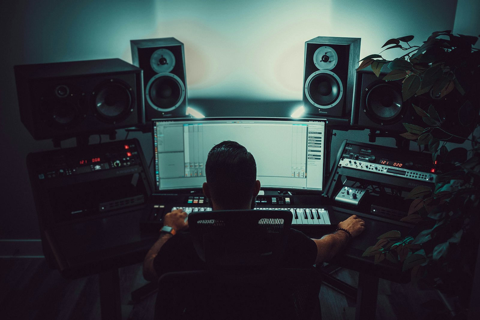 A person at a studio desk facing monitors and a mixing controller.