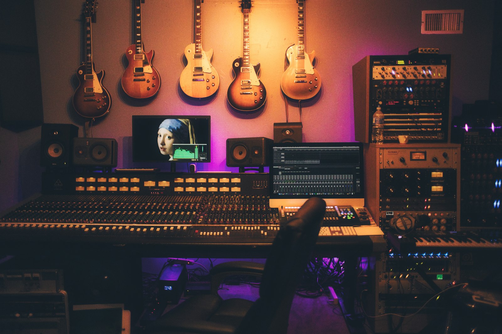 A recording studio with a mixing desk, monitors, and guitars on the wall.